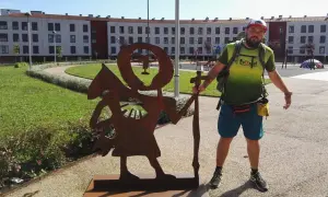 Pielgrzym na camino de santiago pozuje obok rdzewiejącej rzeźby pielgrzyma.