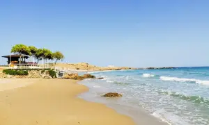 Piękne zakynthos plaże z piaszczystym brzegiem, turkusową wodą i kamienistymi wysepkami. W oddali widać biały domek i zielone drzewa.