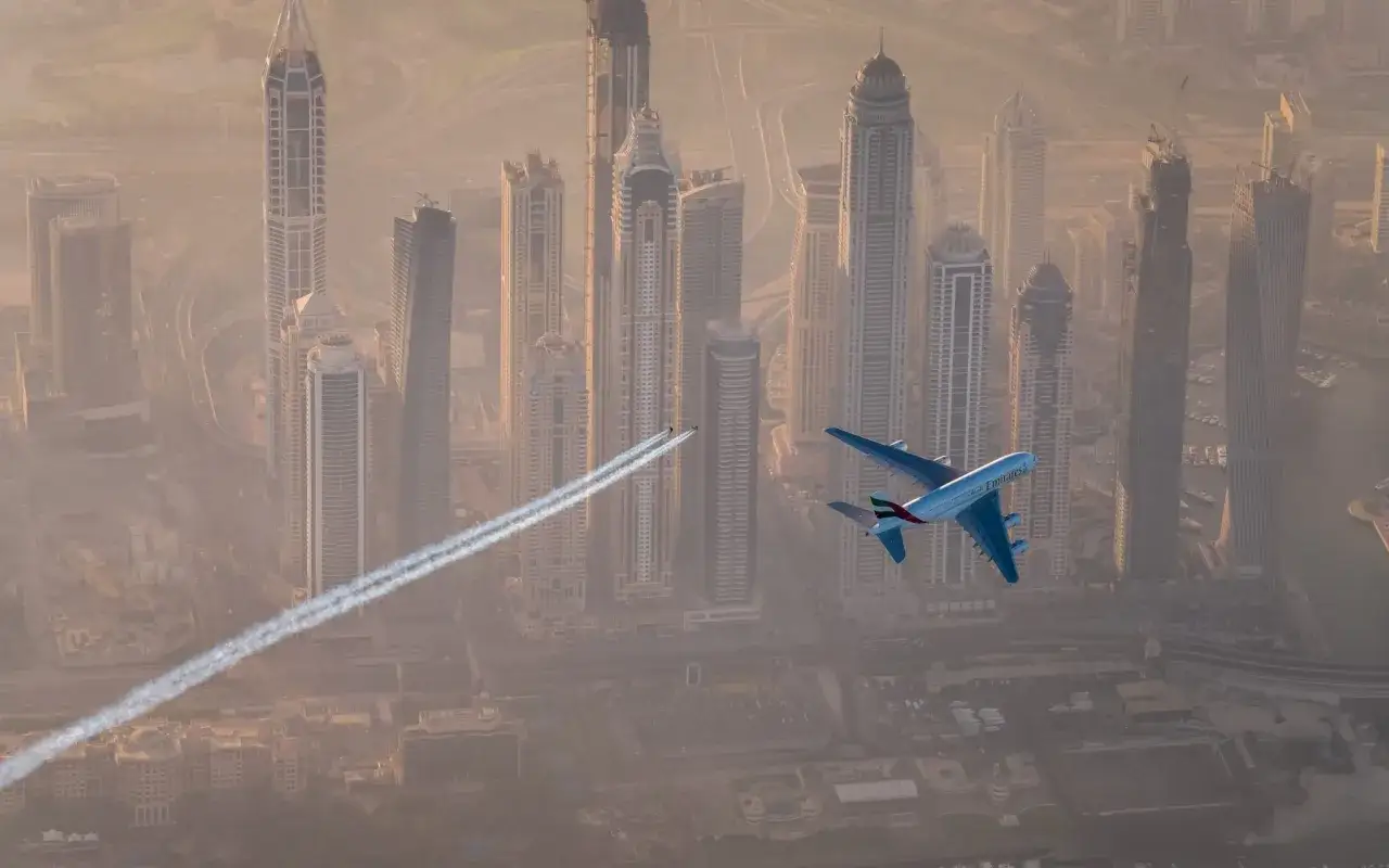 Samolot Emirates leci nad Dubajem, zostawiając smugę kondensacyjną. Zastanawiasz się, ile trwa lot do Dubaju?